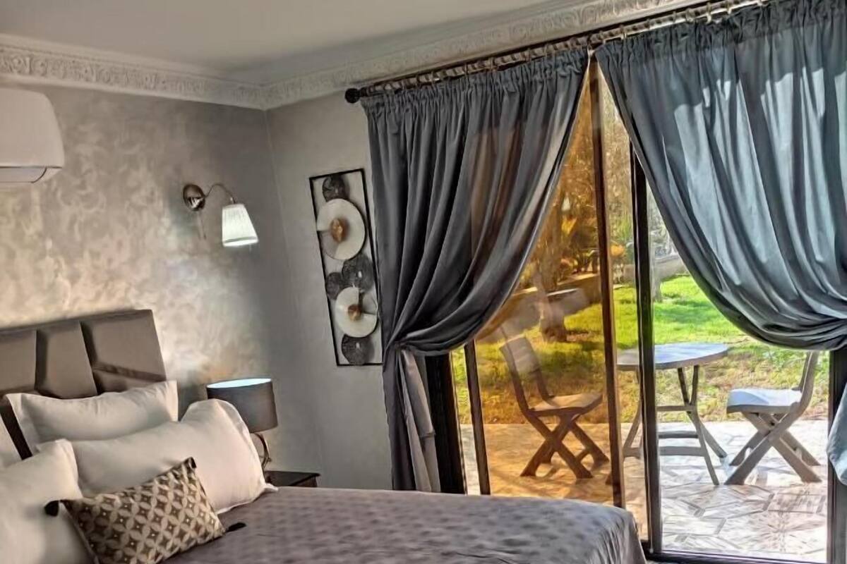 A bedroom with a large bed, a nightstand, a wall-mounted lamp, and a view of an outdoor patio.