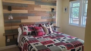 Un dormitorio con cabecera de madera, edredón acolchado con estampados de animales, lámparas de noche y ventana con vistas.