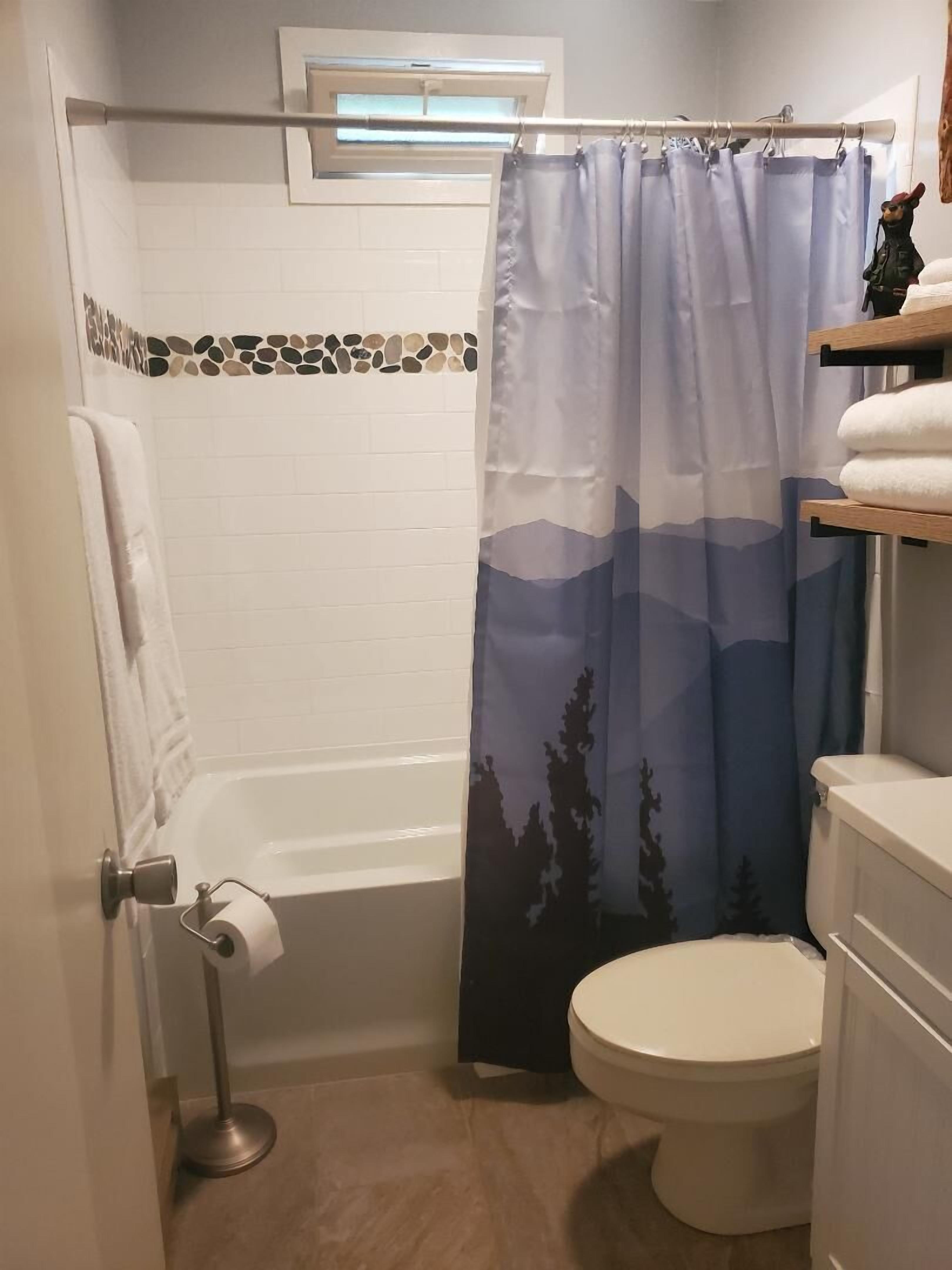A bathroom with a bathtub, toilet, and a shower curtain with a mountain design.