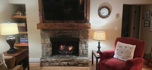 A cozy living room with a stone fireplace, a red armchair, and a television mounted above the fireplace.