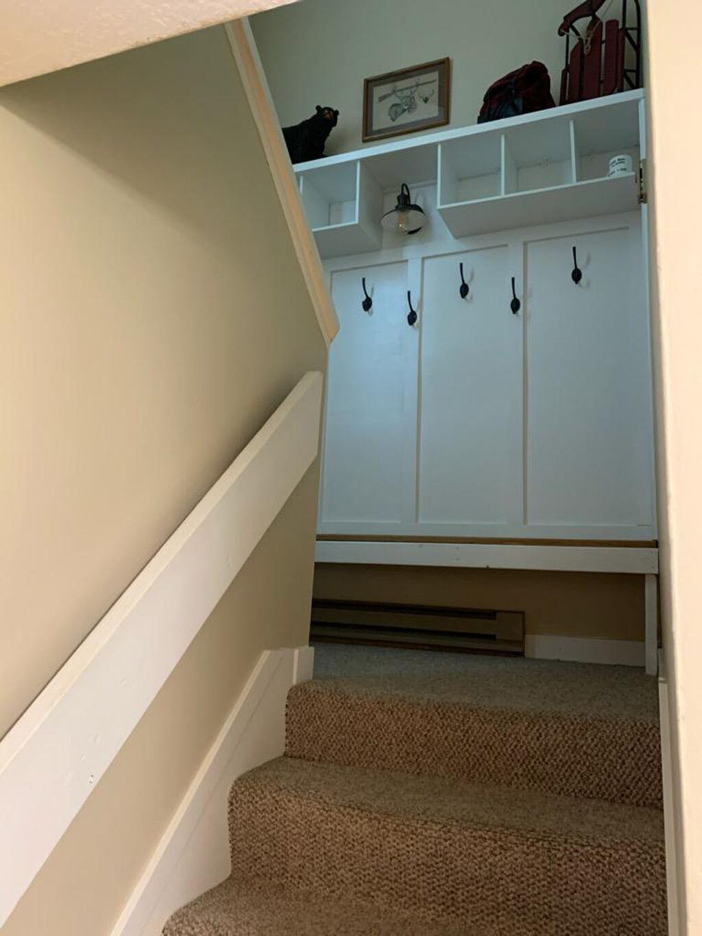 Una escalera que conduce a un espacio de almacenamiento blanco con varios ganchos y un cuadro en la pared.