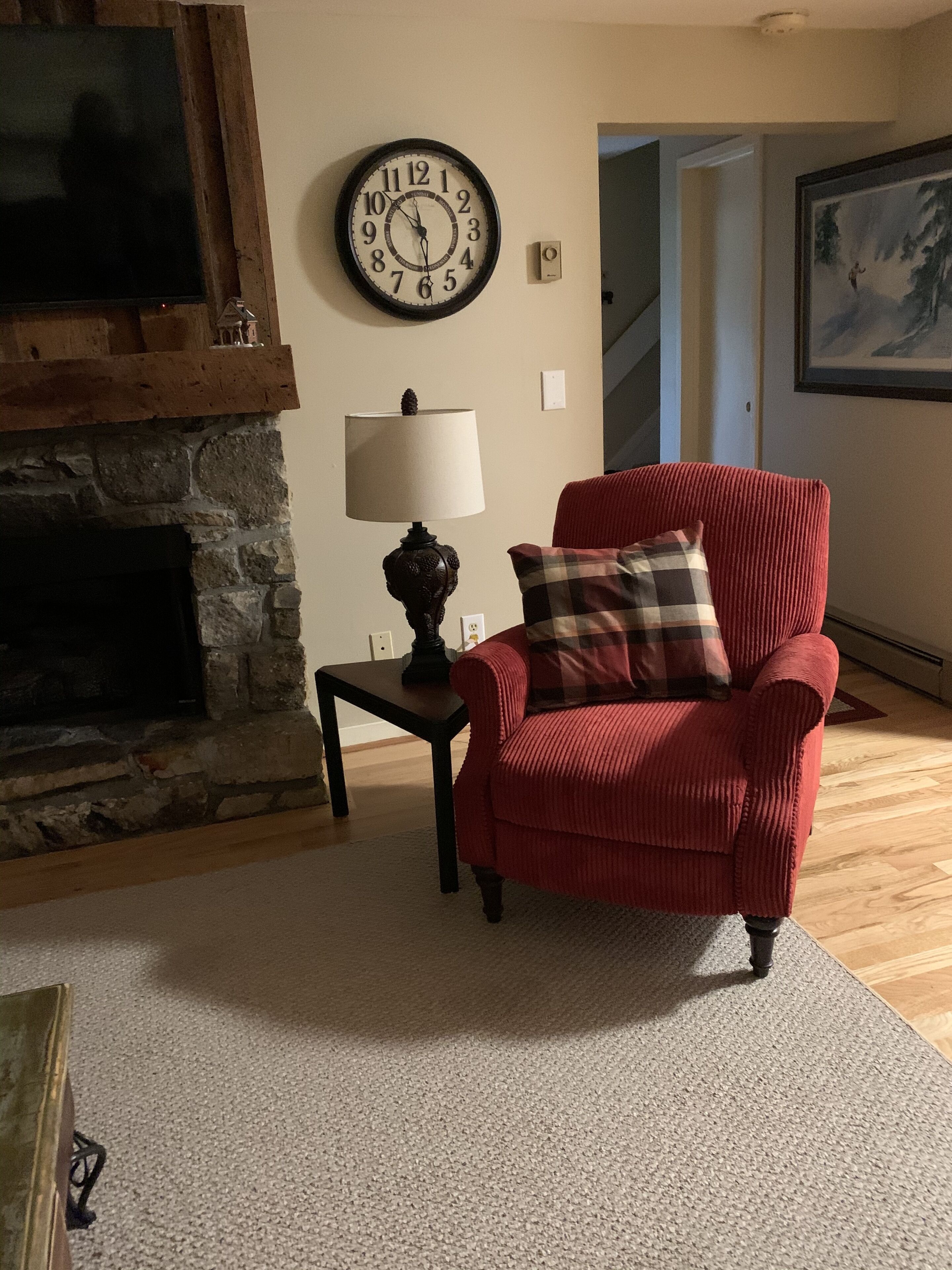 A living room with a fireplace, a red armchair, a clock, and a lamp.