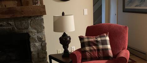 A living room with a fireplace, a red armchair, a clock, and a lamp.