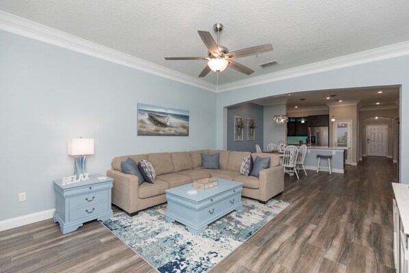 A living room with a beige sectional sofa, a blue coffee table, and a ceiling fan.