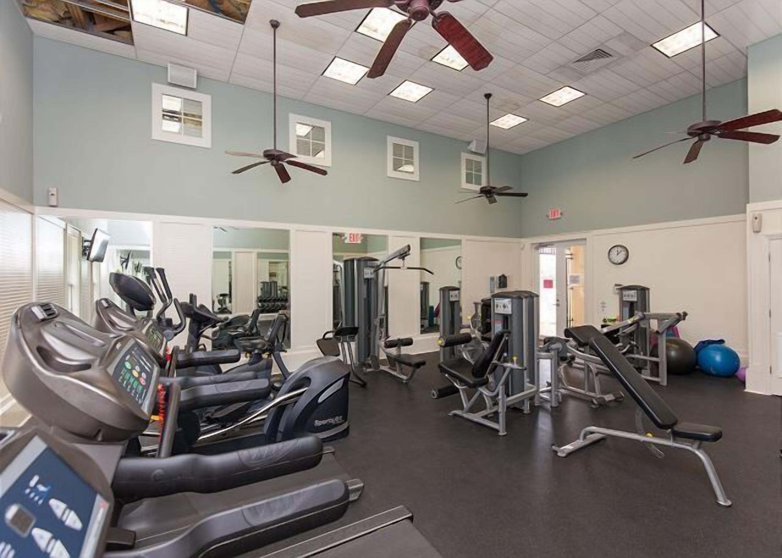 A gym with treadmills, weight machines, and ceiling fans.