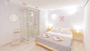 A bedroom with a bed, a glass shower enclosure, a bedside table, and a wall-mounted light fixture. - SunCastle Romantic Loft (Alicante/Alacant)