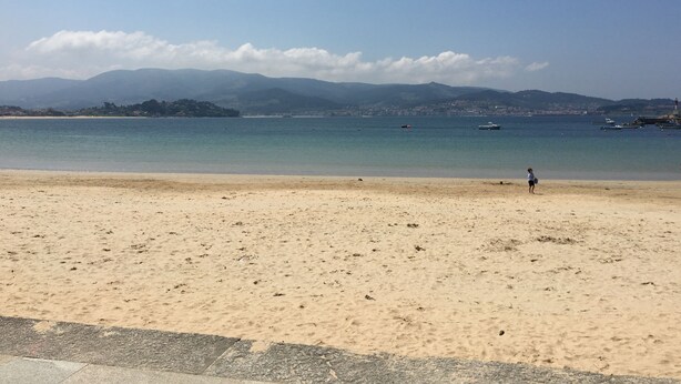 A beach with a clear sky, calm sea, and distant mountains.