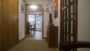 A hallway with wooden doors, a dining area with a table and chairs, and a decorative vase with branches.