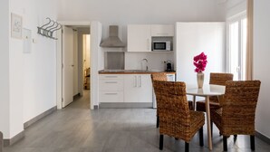 A modern kitchen with white cabinets, a microwave, and a stainless steel range hood. There is a dining area with wicker chairs and a white table, and a vase with pink flowers. - Sanlúcar de Barrameda  4 (Sanlucar de Barrameda)