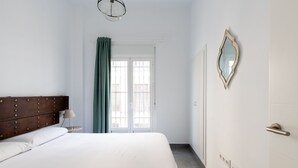 A bedroom with a large bed, a wooden headboard, a nightstand, a lamp, a mirror, and a door with a window. - Sanlúcar de Barrameda  4 (Sanlucar de Barrameda)
