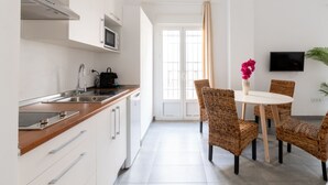 A modern kitchen with white cabinets, a stainless steel sink, and a microwave. There is a dining area with wicker chairs and a white table, and a TV mounted on the wall. - Sanlúcar de Barrameda  4 (Sanlucar de Barrameda)