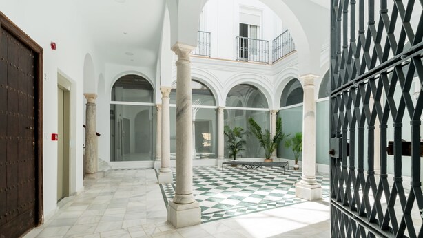A spacious atrium with high ceilings, a checkered floor, and a central open area with columns and potted plants.