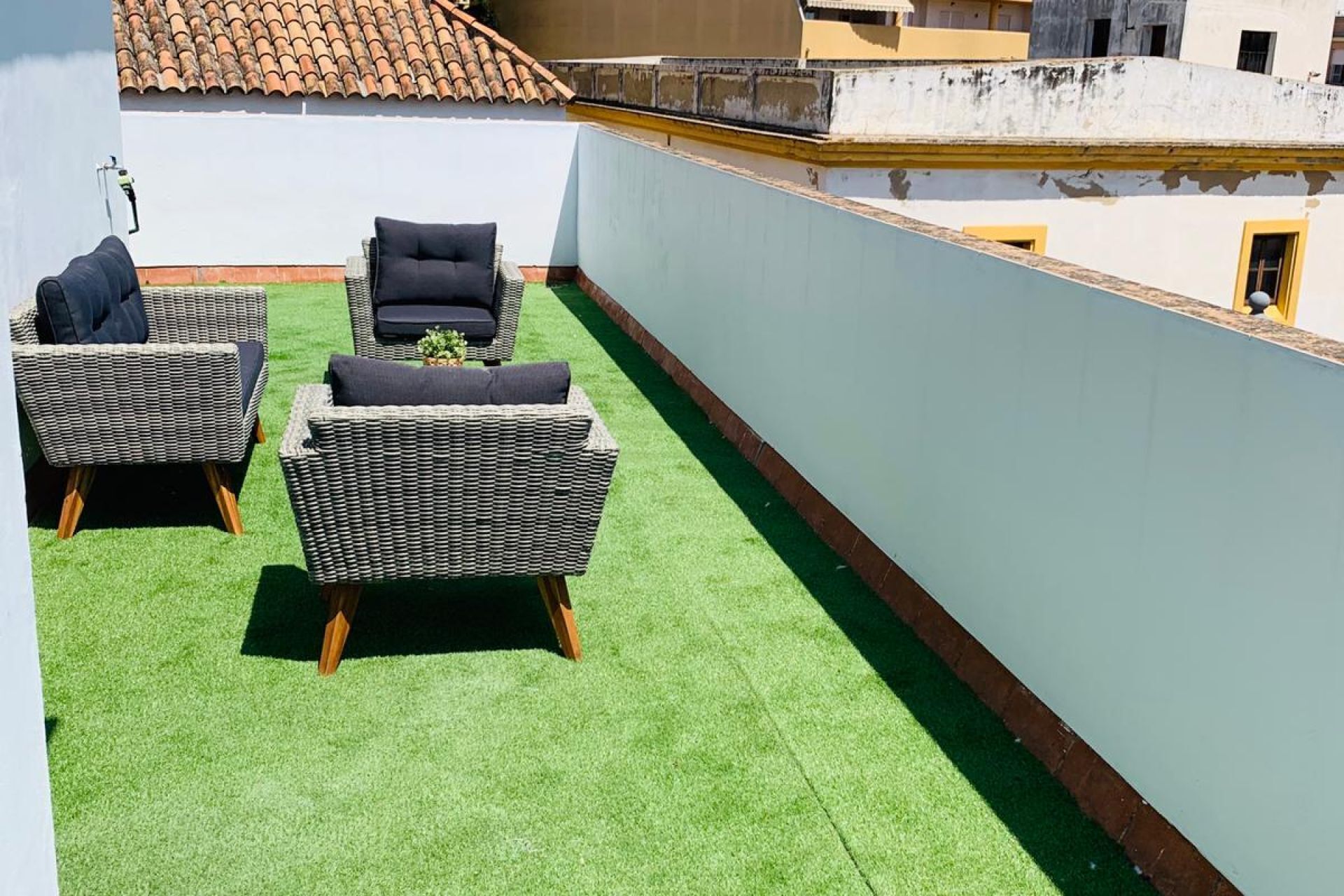 Een dak terras met twee rieten zitbanken en een kleine tafel, omringd door kunstgras.