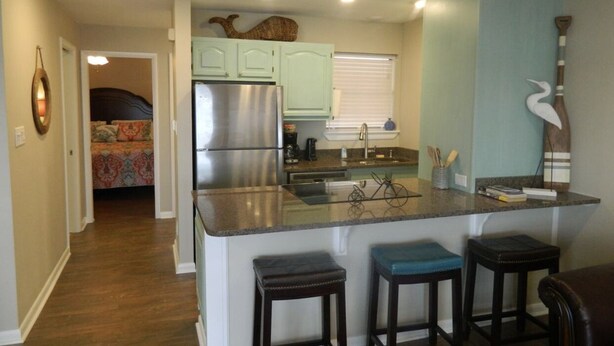 Cocina compacta con refrigerador, lavamanos y un comedor con taburetes.