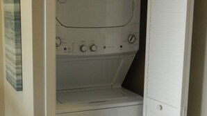Un lavadero pequeño con lavadora y secadora, un estante y una puerta con picaporte.
