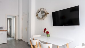 A modern dining area with a white table, four white chairs, a flat-screen TV, and a decorative mirror. - Sanlúcar de Barrameda  6 (Sanlucar de Barrameda)