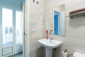 A bathroom with a white sink, a mirror, and a toilet. There is a window with a view of a balcony. - Sanlúcar de Barrameda  6 (Sanlucar de Barrameda)