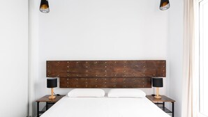 A neatly made bed with a wooden headboard, two bedside tables with lamps, and a plain white wall. - Sanlúcar de Barrameda  6 (Sanlucar de Barrameda)