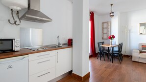 A compact kitchen with a microwave, sink, and stainless steel range hood. A dining area with a table and chairs is visible, featuring a vase with flowers.