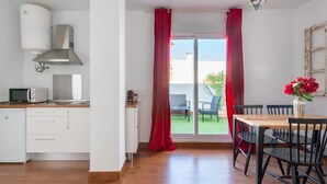 A modern kitchen with white cabinets, a microwave, and a stove. There is a dining area with a table and chairs, and a red curtain.