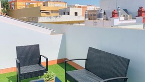 A rooftop terrace with two wicker chairs, a small potted plant, and a view of surrounding buildings.