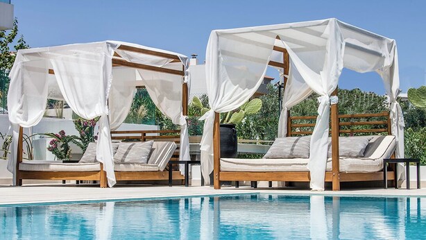 Two wooden beds with white canopies, a pool, and greenery in the background. - King Suite with privat jacuzzi (rethymno)