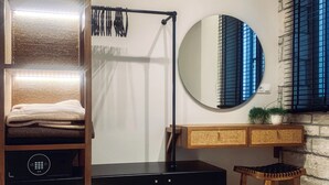 A bedroom with a bed, a vanity with a mirror, a stool, a wardrobe, and a wall-mounted light fixture. - King Suite with privat jacuzzi (rethymno)
