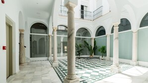 A spacious atrium with high ceilings, classical columns, and a checkered floor pattern.