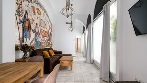 A spacious living area with a large mural, a wooden table, a sofa, and a TV mounted on the wall.