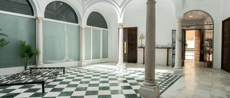 Un vestíbulo amplio con suelo de cuadros, techos altos y arquitectura clásica que incluye columnas y arcos.