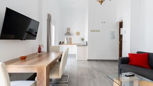 Una sala de estar moderna con una mesa de comedor de madera, una mesa de centro de vidrio y un sofá gris con un cojín rojo.