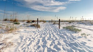 Een zanderig strand met een houten hek en schaarse begroeiing.