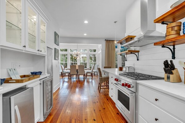 A modern kitchen with white cabinetry, a stainless steel refrigerator, a gas stove, and wooden shelves. - Bright Getaway Near Beach and Pools (Santa Rosa Beach)