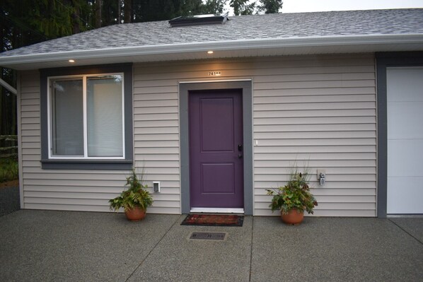 A single-story house with a purple front door, two potted plants, and a garage door.