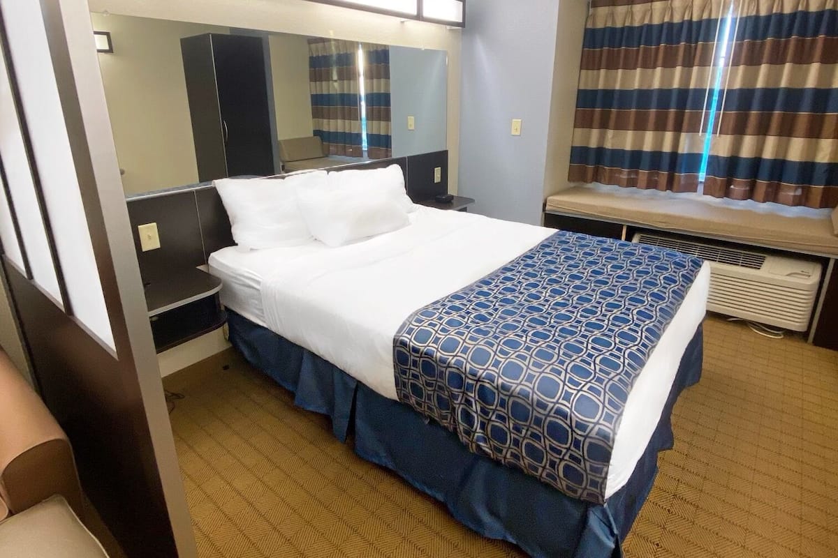 A hotel room with a large bed, a desk, a chair, a mirror, and a window with curtains.