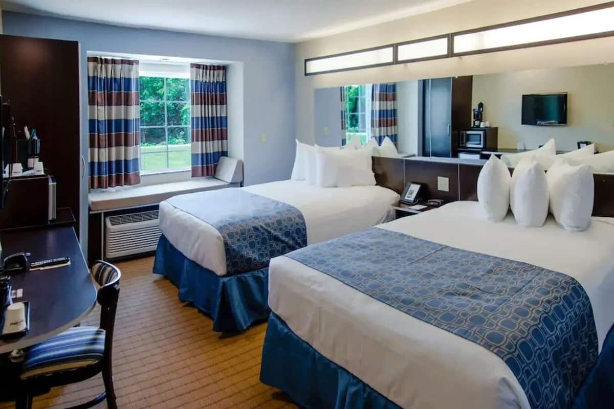 A hotel room with two beds, a desk, a chair, a TV, and a window with curtains.