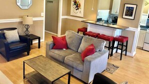 A living room with a sofa, a coffee table, a chair, and a red bar stool. - Easy Walk to Downtown Attractions & WORLD CUP! (Atlanta)