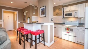 A modern kitchen with white cabinets, a central island with red bar stools, and a microwave above the stove. - Easy Walk to Downtown Attractions & WORLD CUP! (Atlanta)