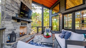 A stone fireplace with a TV, a wooden deck, and a white sofa with patterned cushions. - Somethin 2 Talk About ("S2TA") (McCurtain County)