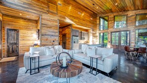 A spacious living area with a large white sectional sofa, a round coffee table, and a dining area with wooden chairs. - Somethin 2 Talk About ("S2TA") (McCurtain County)