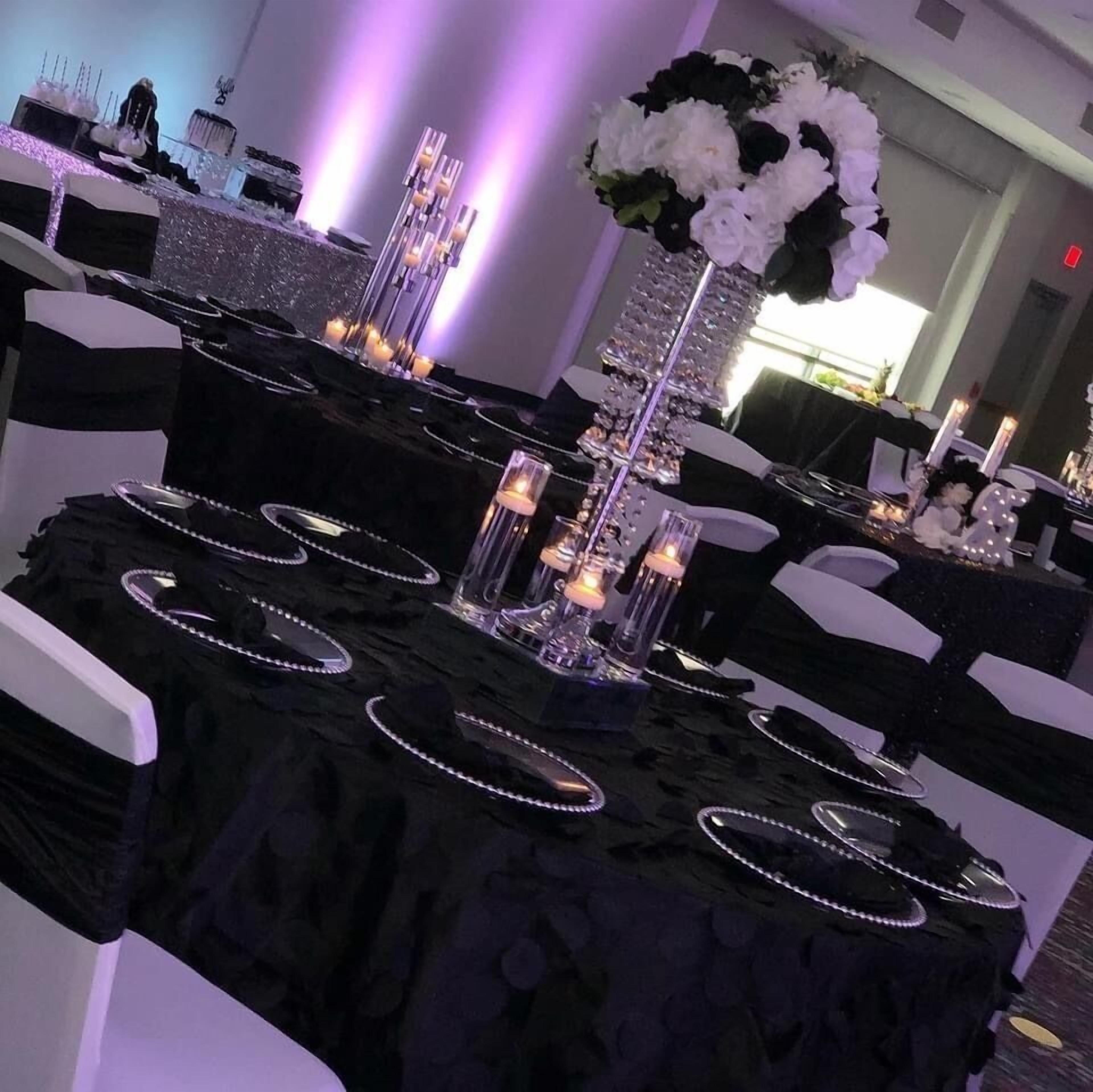 A banquet hall with round tables covered in black tablecloths, white chairs, and decorative candle holders.