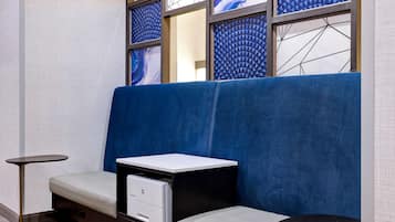 Quarto de hotel moderno com um sofá estofado azul, uma mesinha lateral e uma impressora embutida.