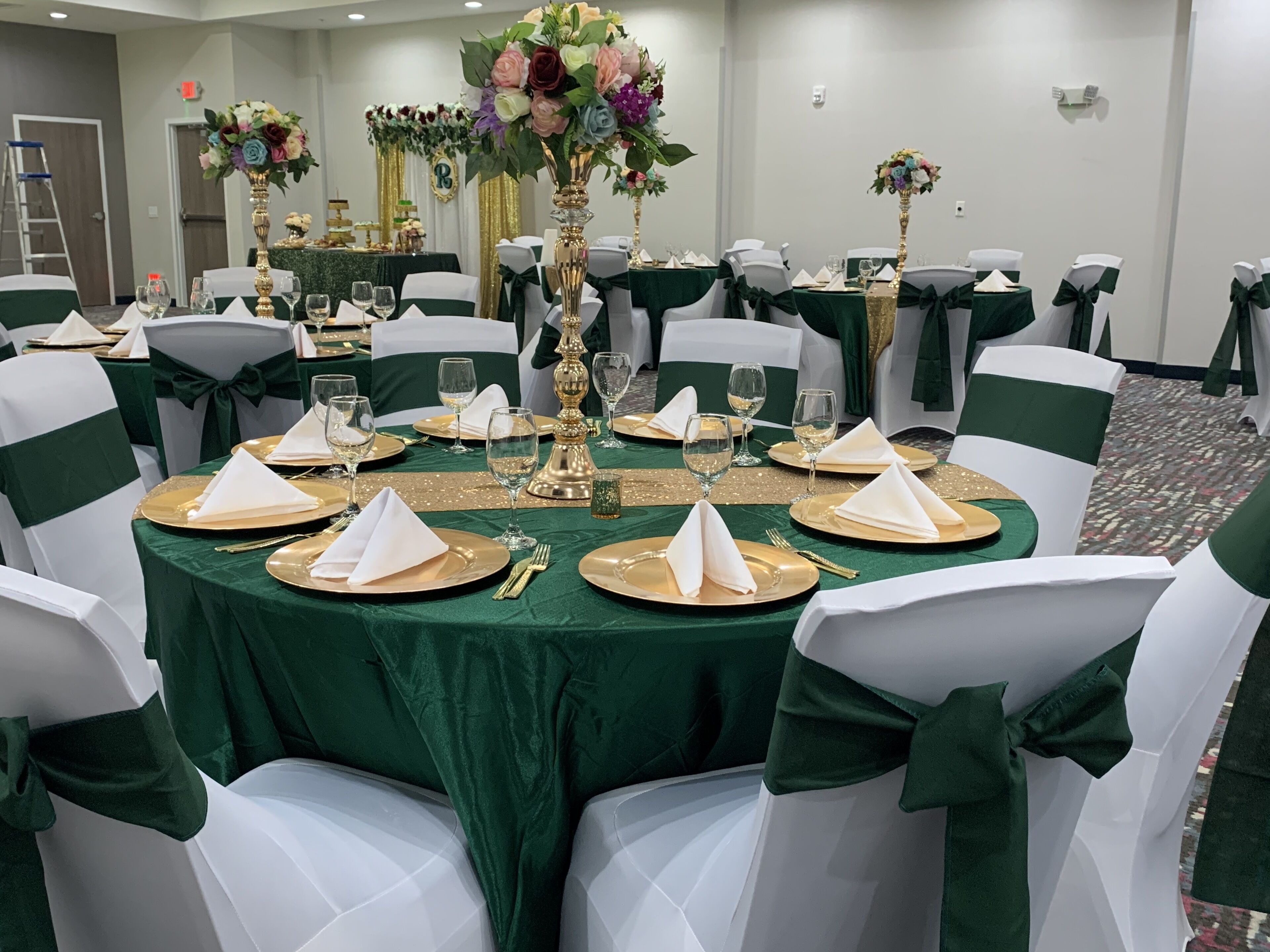 Une salle de banquet avec des tables rondes recouvertes de nappes vertes, des chaises blanches ornées de rubans verts et des touches dorées.