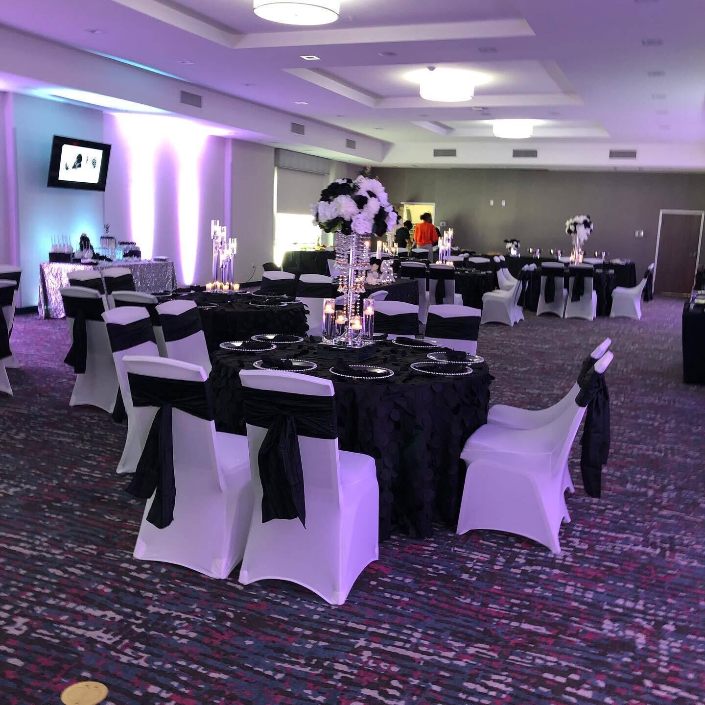 A banquet hall with round tables, white chairs, and black tablecloths.