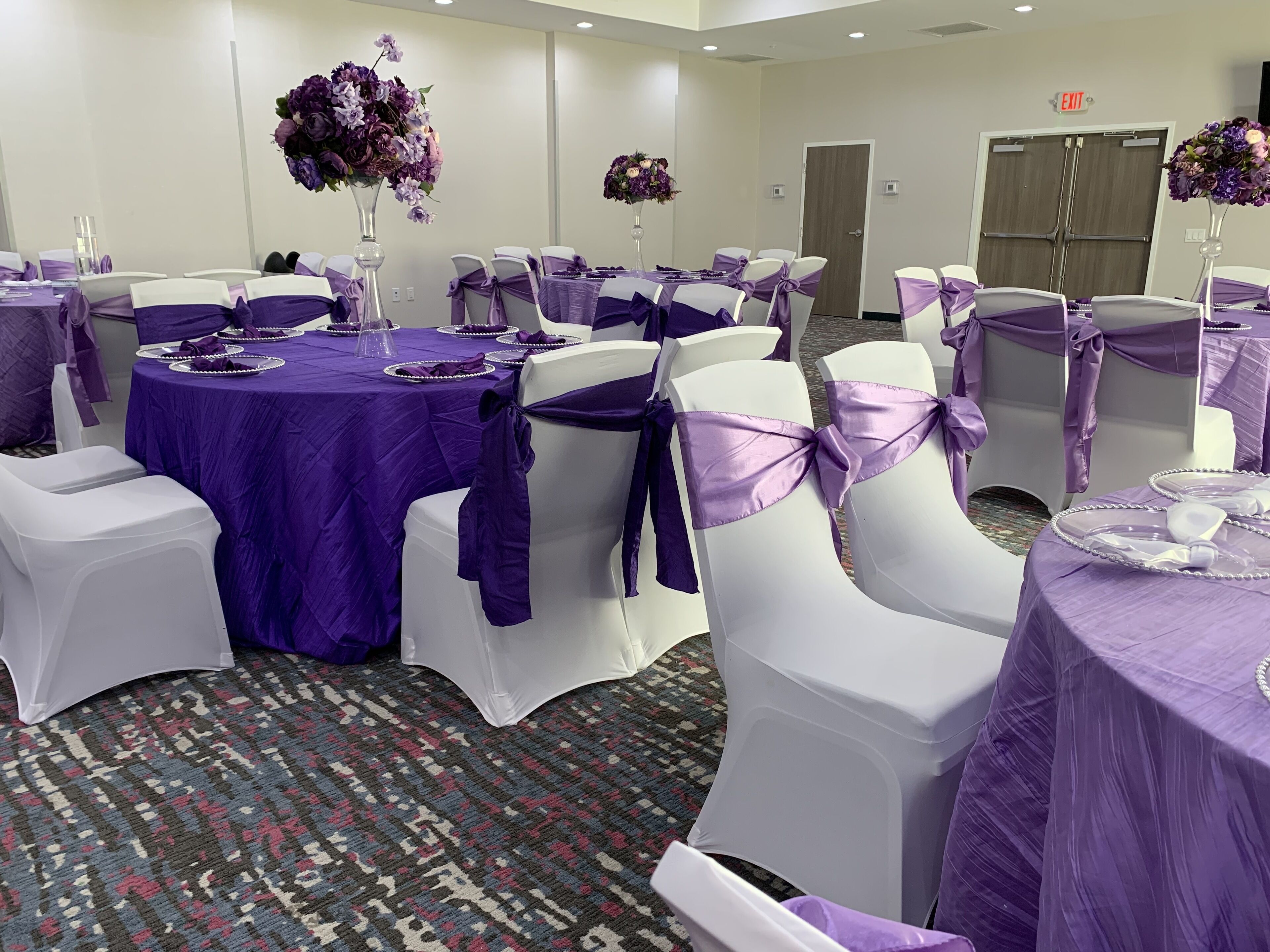 A conference room with round tables, white chairs, and purple tablecloths.