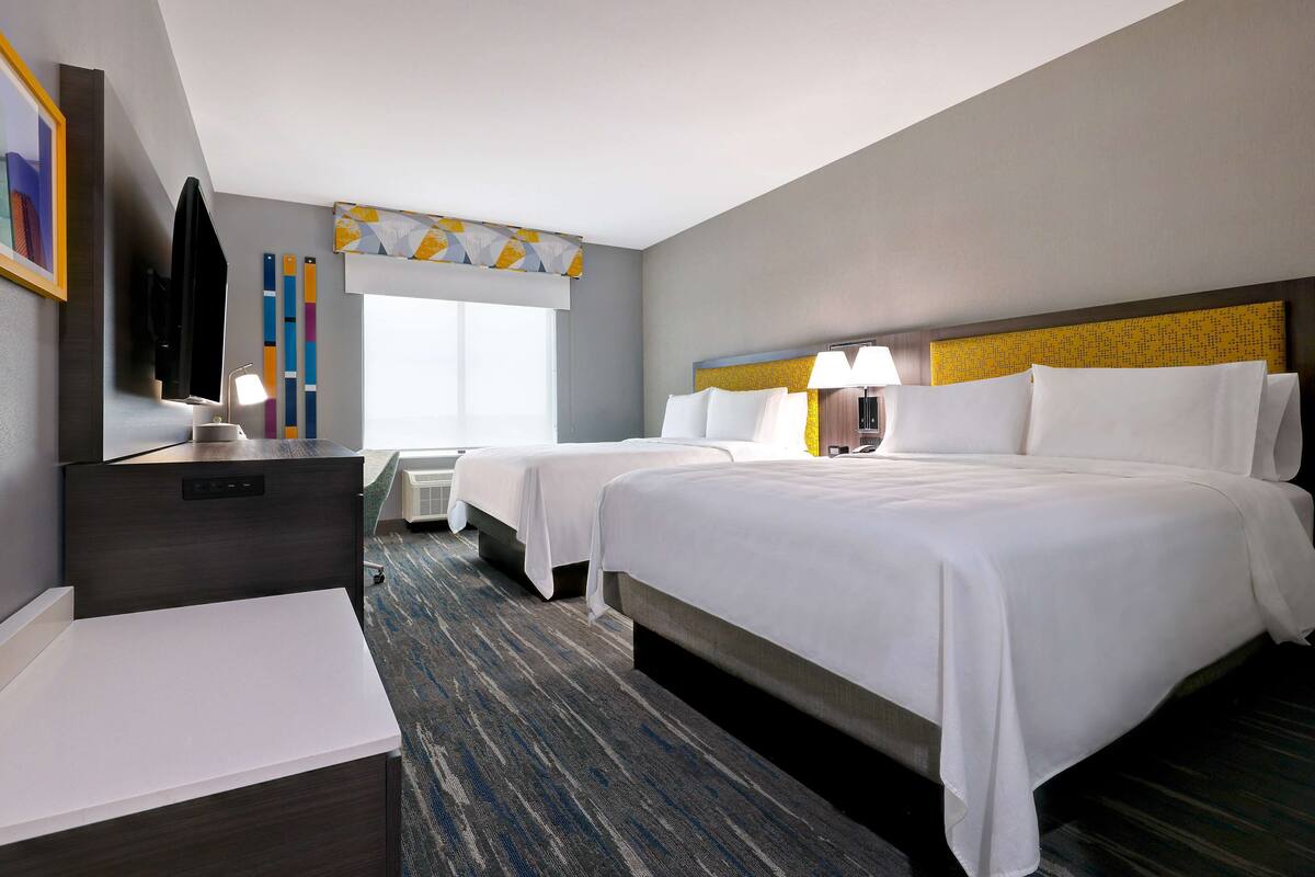 A hotel room with two beds, a desk, a chair, a TV, and a window with curtains.