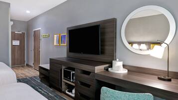 Habitación de hotel moderna con un televisor de pantalla plana grande, un espejo redondo, un escritorio con lámpara y una cama con alfombra azul y gris a rayas.