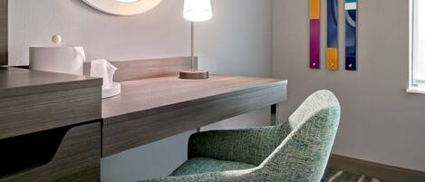Un baño moderno con tocador de madera, un espejo redondo, dispensador de toallas blanco, una lámpara de pie y una silla verde.