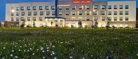 A Hampton Inn & Suites hotel with a modern design, featuring multiple floors and a well-lit entrance.