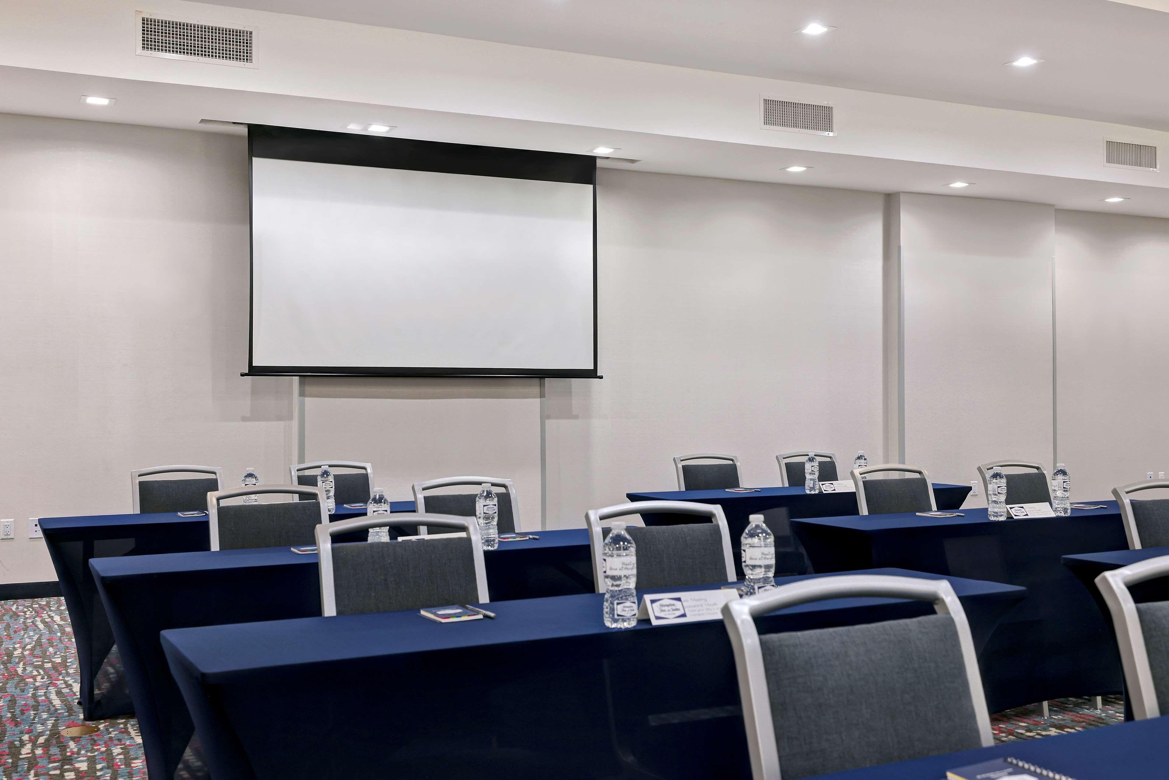 Un salón de conferencias con mesas, sillas, una pantalla de proyector y tarjetas de identificación.